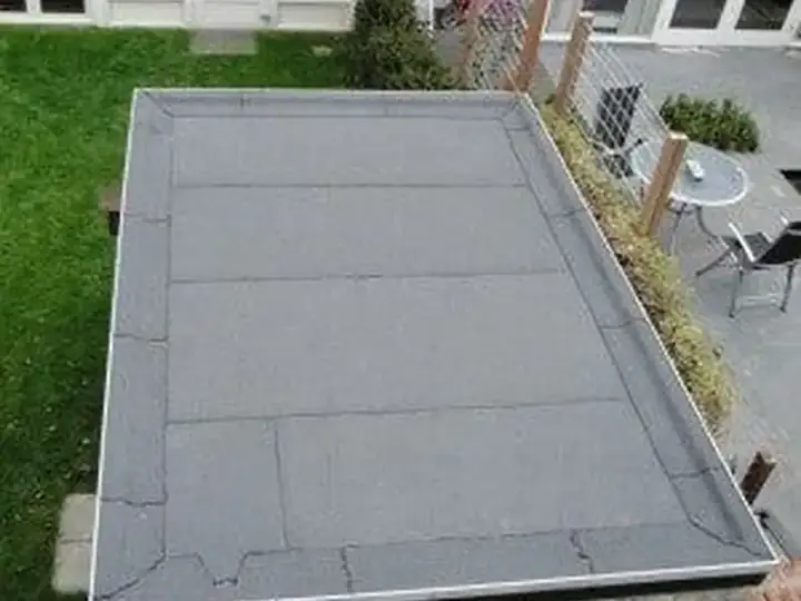 Plat dak van een aanbouw gezien vanaf boven, met lichtkoepel en de tuin eromheen