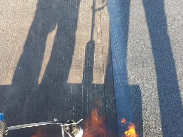 Dakdekker werkt met de brander rond een doorvoer, de vlam is zichtbaar