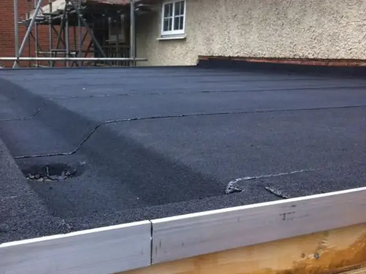 Plat dak van een aanbouw met steiger eromheen en nieuwe zwarte dakbedekking op een houten dakrand